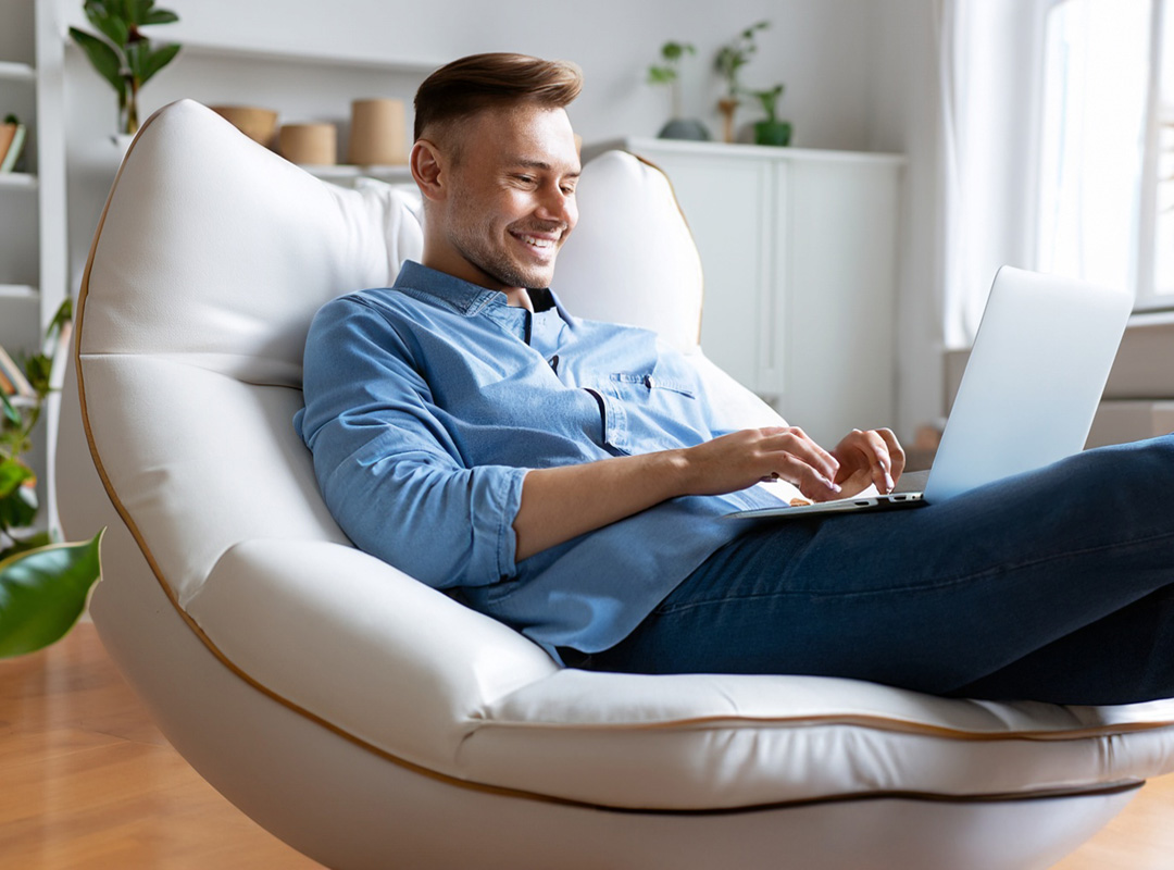 Zadowolony ze strony internetowej klient pracuje z laptopem siedząc na kanapie w domu.